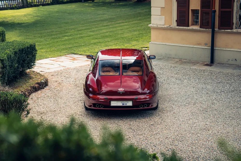 Voiture rouge Spyker C8 Preliator garée sur gravier devant une maison, vue arrière.