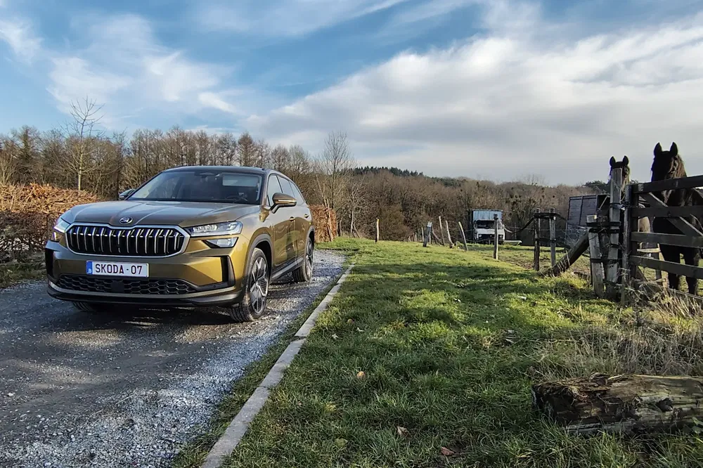 SUV Skoda sur chemin de campagne, ciel bleu avec nuages, chevaux à proximité.