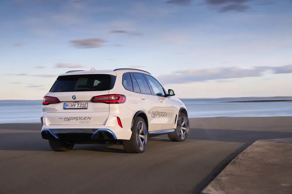 BMW iX5 Hydrogen rijdt langs het water bij zonsondergang, baanbrekend waterstofvoertuig.