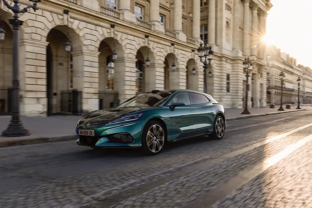 MG 5 électrique roule sur une route pavée devant un bâtiment historique élégant.