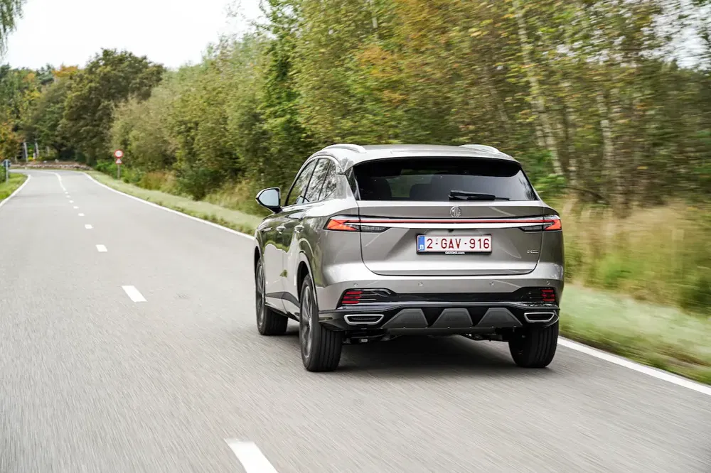 SUV moderne argenté roule sur route bordée d'arbres en Belgique.