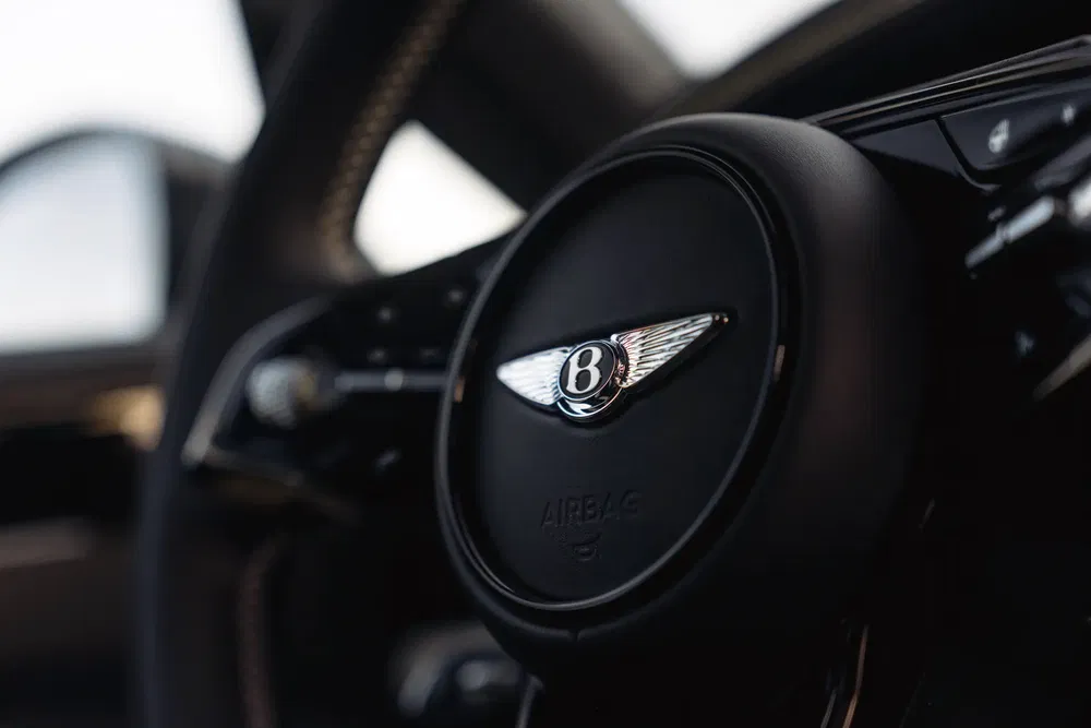 Volant de voiture Bentley avec logo ailé, intérieur de luxe en gros plan.