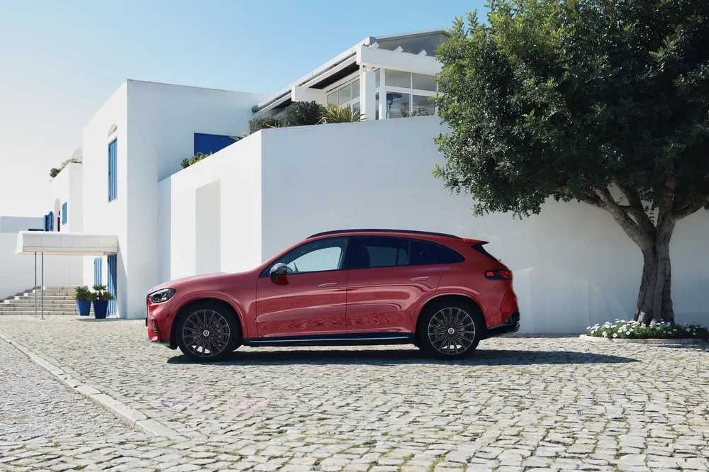 Rode Mercedes-Benz SUV geparkeerd voor moderne witte huizen, schaduwrijke boom aan de zijkant.