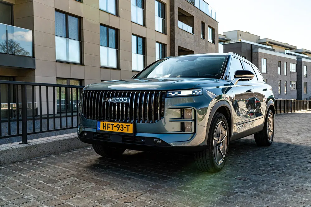 Moderne JAECOO SUV geparkeerd voor een stijlvol wooncomplex, natuurlijk ochtendlicht.