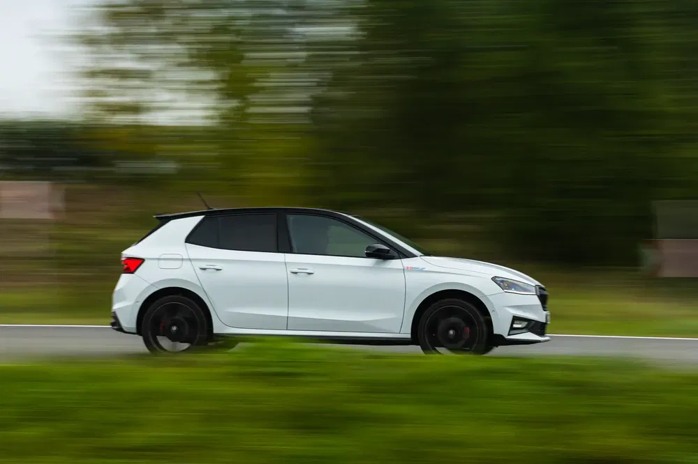 Skoda Fabia blanche roulant rapidement sur une route bordée de végétation floue.