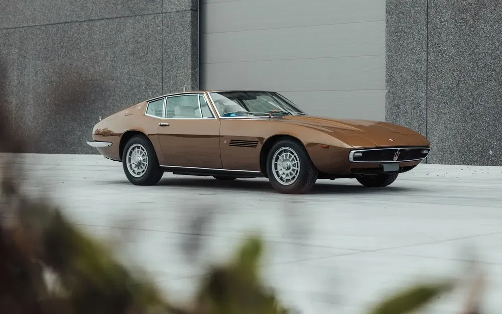 Maserati Ghibli brun, voiture classique stationnée devant un mur de béton
