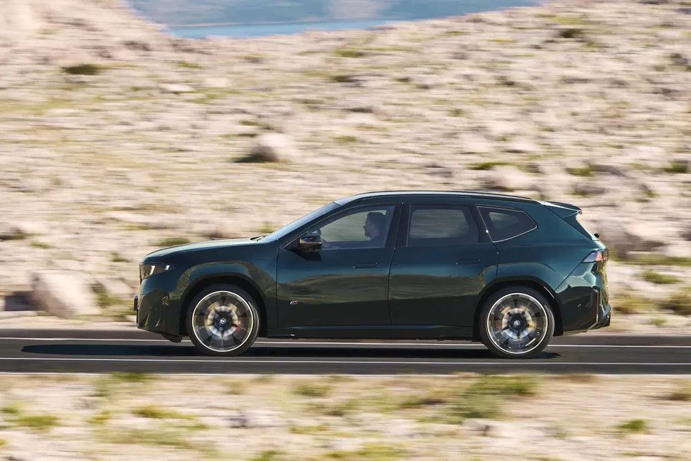 BMW iX vert roulant sur une route, paysage désertique en arrière-plan.