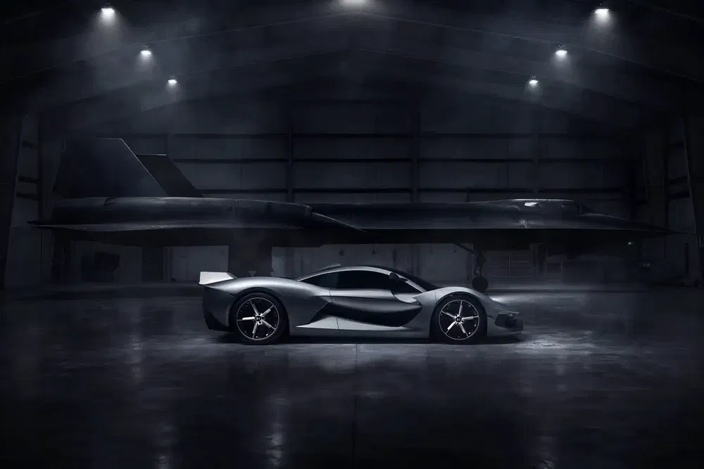 Hypercar Czinger 21C grise dans un hangar avec avion furtif en arrière-plan.