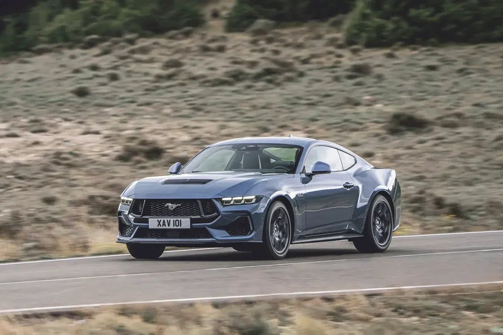 Ford Mustang GT grise roulant sur une route déserte, performance sportive et design élégant.