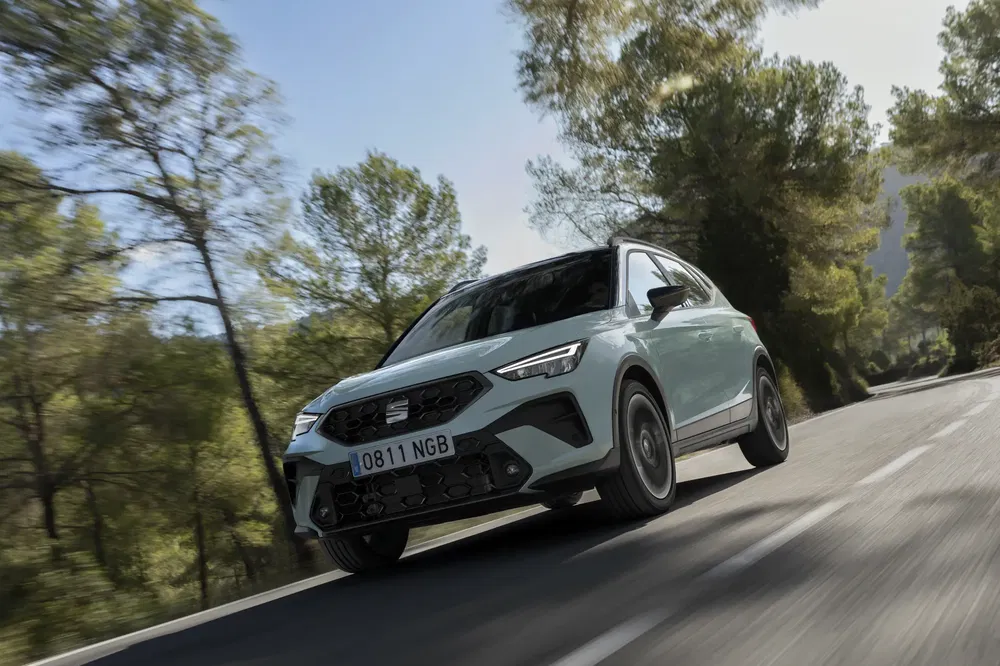 SEAT Arona dynamique sur route bordée d'arbres, ciel clair en arrière-plan.