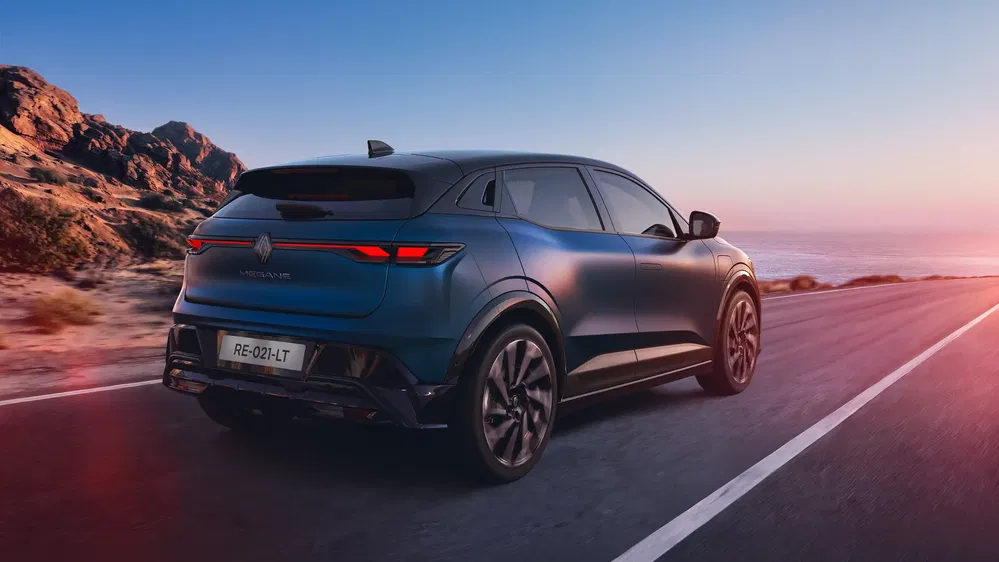 Renault Mégane E-Tech rijdt langs een kustweg bij zonsondergang.