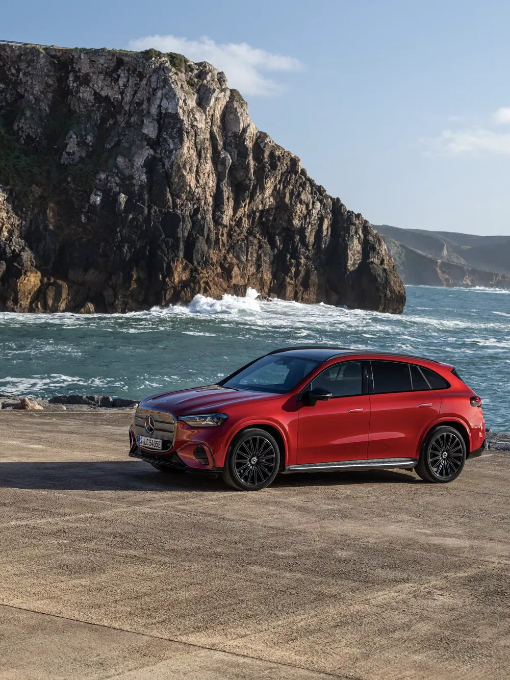 Rode Mercedes-Benz SUV aan een ruige kust, met woelige zee op de achtergrond.