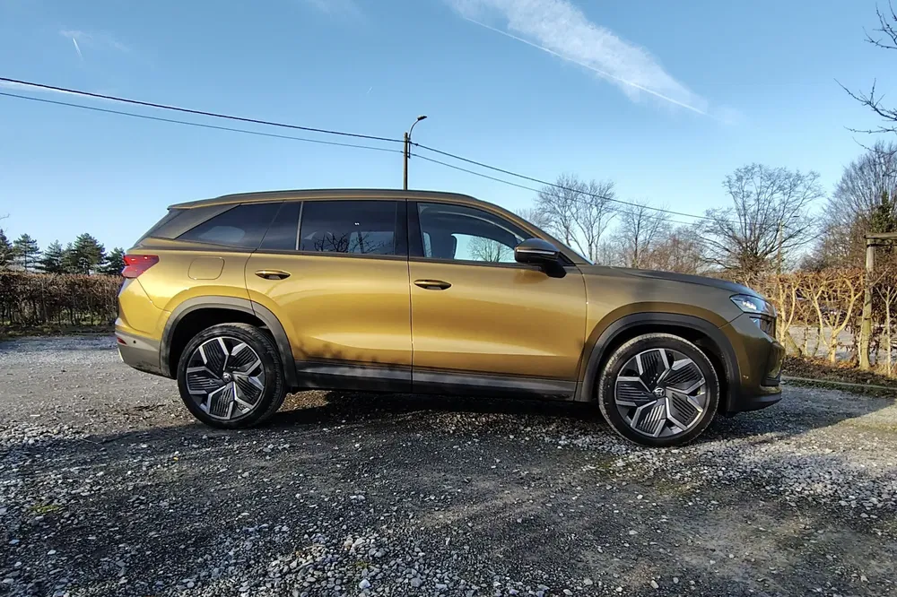 SUV doré stationné au soleil, roues élégantes et design moderne, paysage arrière tranquille.
