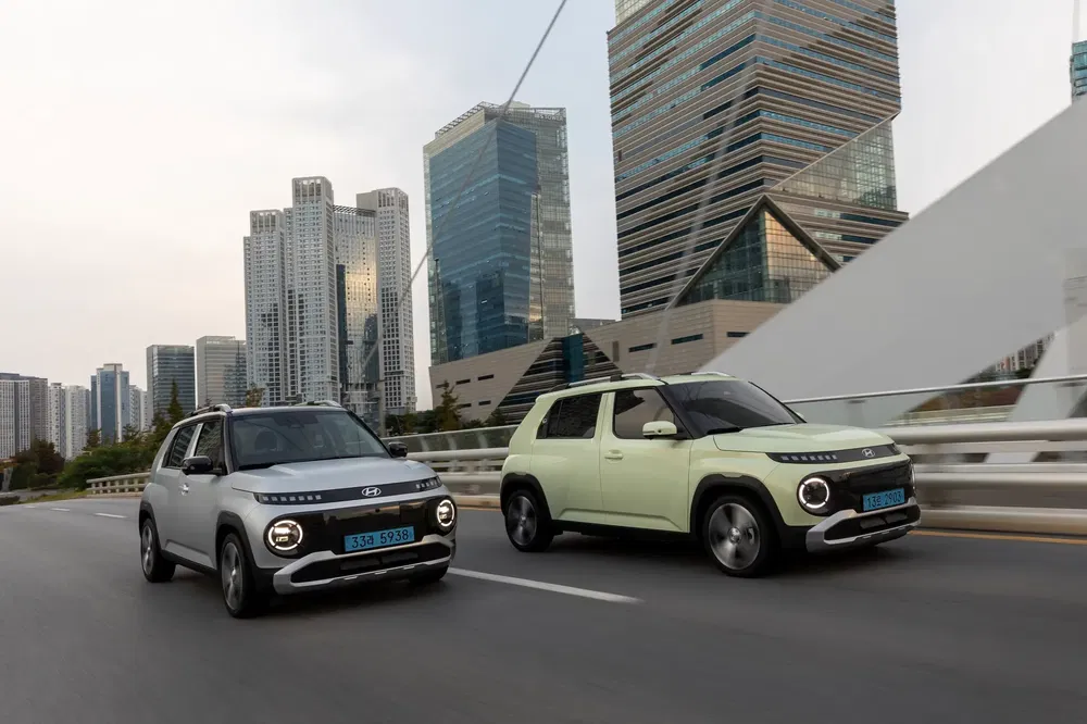 Twee Hyundai Caspers rijden door een stad met moderne wolkenkrabbers.