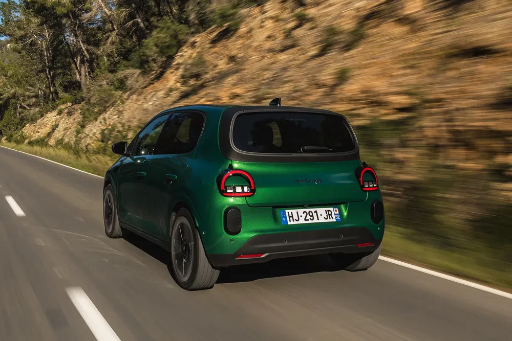 Citroën C3 verte roulant sur une route rurale bordée d'arbres.