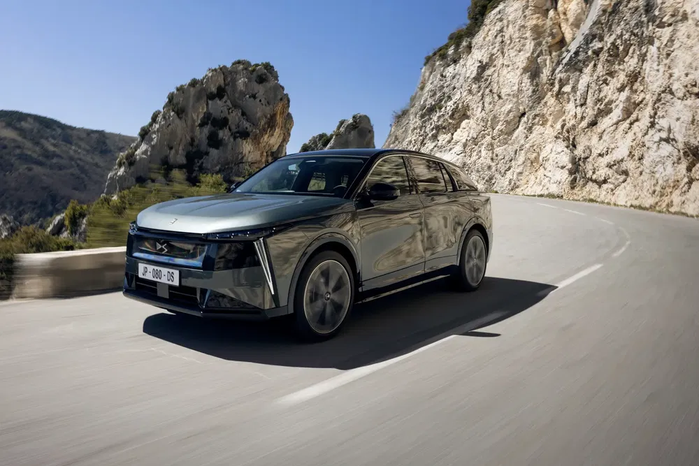 Voiture électrique DS 4 roulant sur une route de montagne sinueuse par temps ensoleillé.