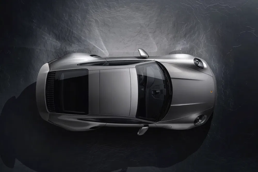 {"fr":"Vue aérienne d'une Porsche 911 argentée sur fond sombre texturé.","nl":"Bovenzicht van een zilveren Porsche 911 op een donkere, textuur achtergrond."}
