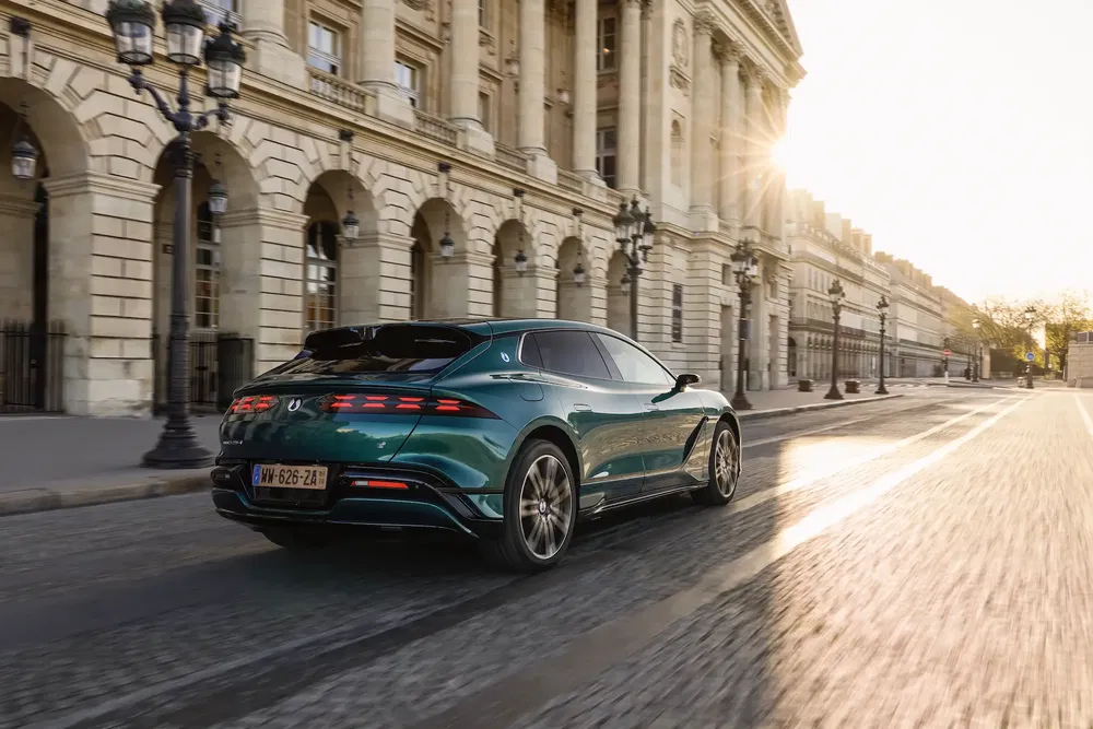 Peugeot 408 vert roulant devant un bâtiment historique au lever du soleil.