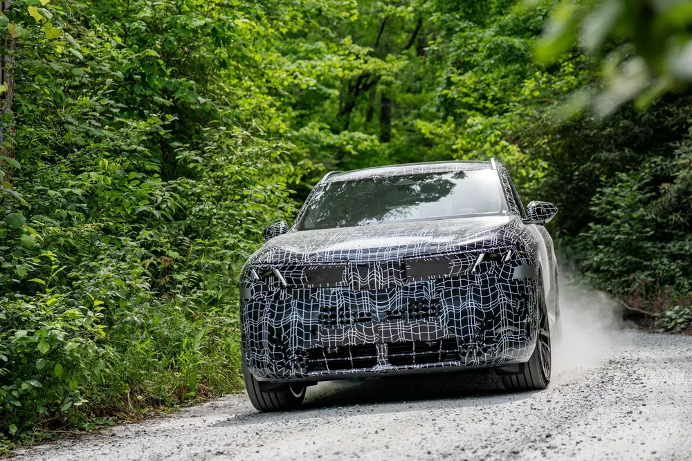 Geheime tests van gecamoufleerde SUV op onverharde weg omringd door dicht bos.