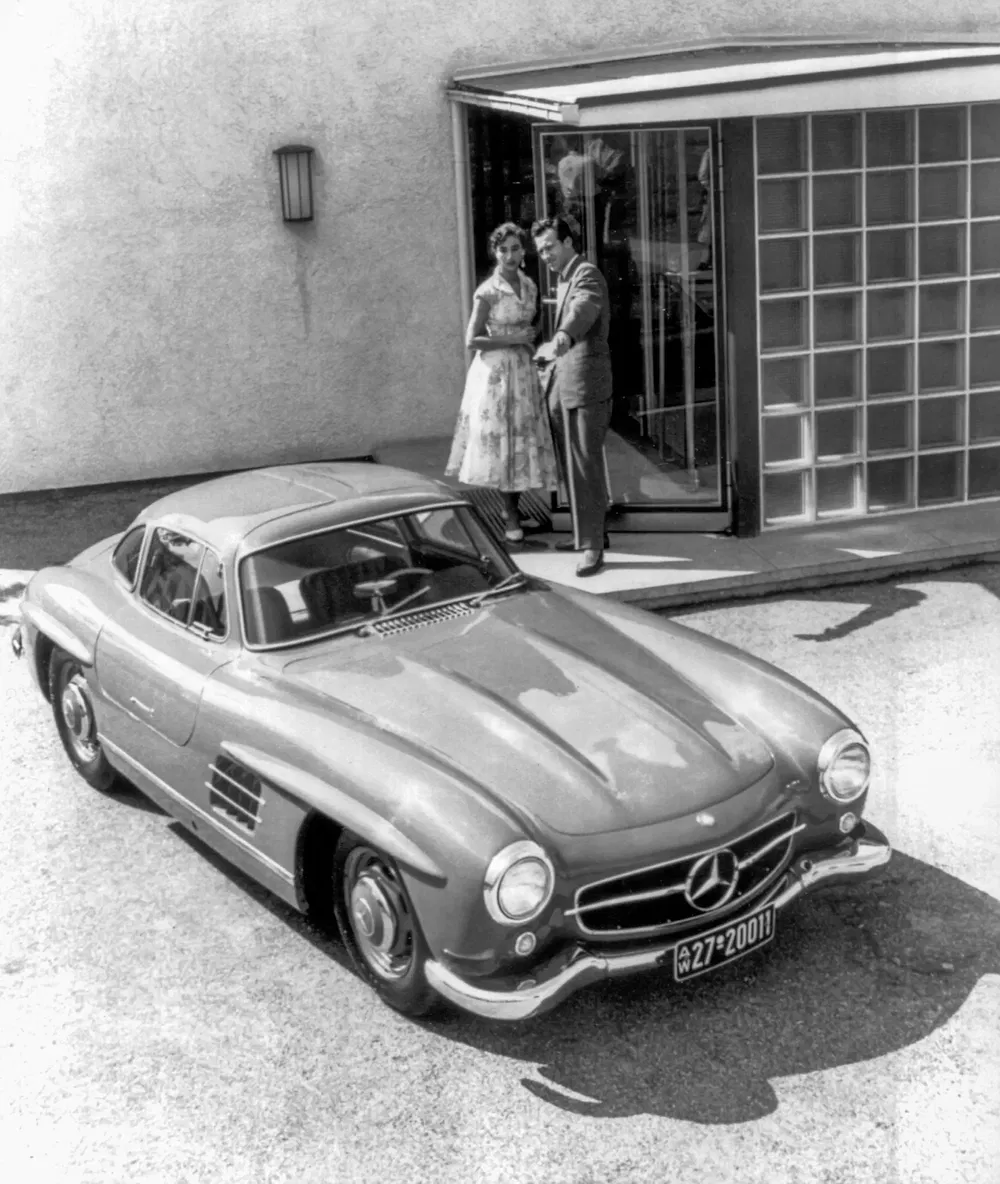 Mercedes-Benz 300SL stationnée devant une maison moderne, couple en arrière-plan.