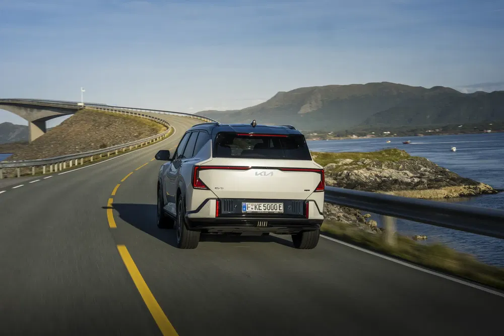 Kia EV9 sur une route côtière sinueuse avec vue sur la mer et les montagnes.