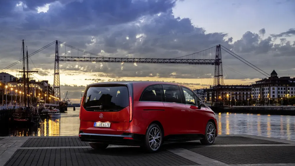 Mercedes Classe V rouge au bord de la rivière, pont industriel à l'arrière-plan au crépuscule.