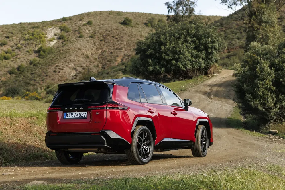 Rode Toyota RAV4 op onverharde weg, bergachtig landschap op de achtergrond.