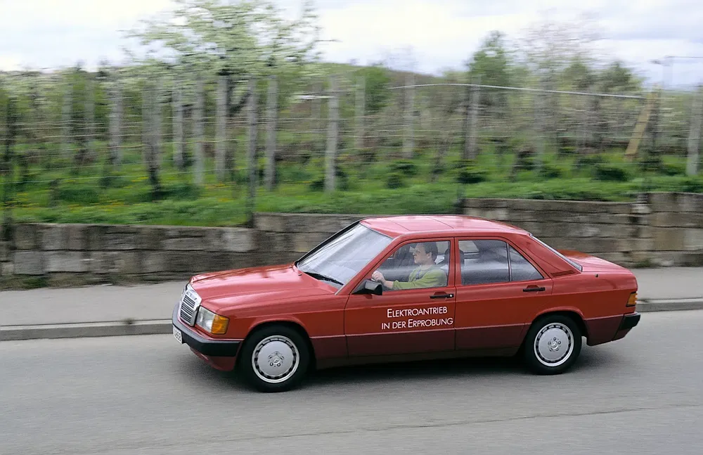 Mercedes-Benz rouge électrique en test routier, paysage verdoyant en arrière-plan.