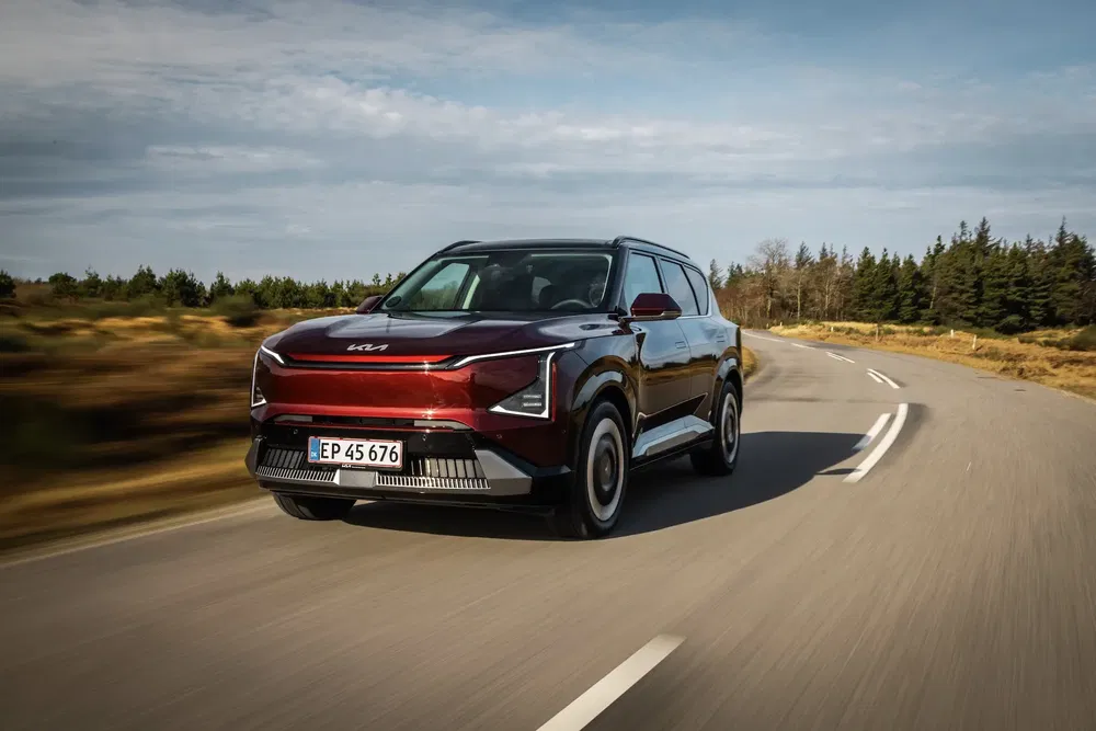 SUV Kia EV9 rouge roulant sur une route sinueuse avec paysage forestier.