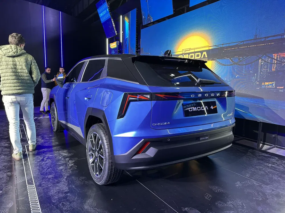 Achteraanzicht van de blauwe Chery Omoda 5 SUV tentoongesteld op verlichte podium met LED-schermen.