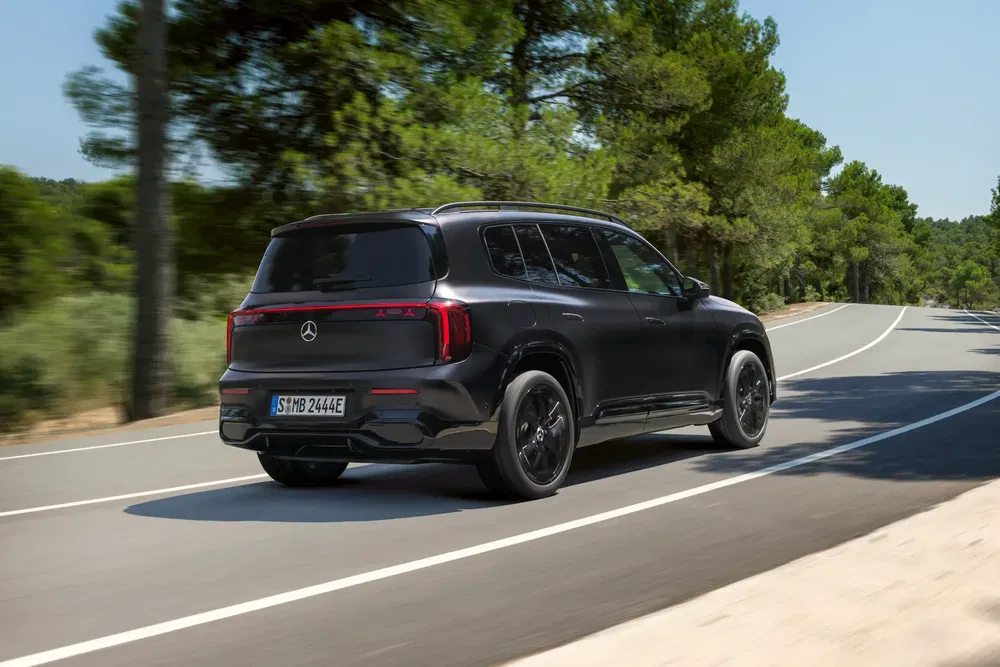 Zwarte Mercedes-Benz EQB rijdt op een weg omringd door bomen bij daglicht.