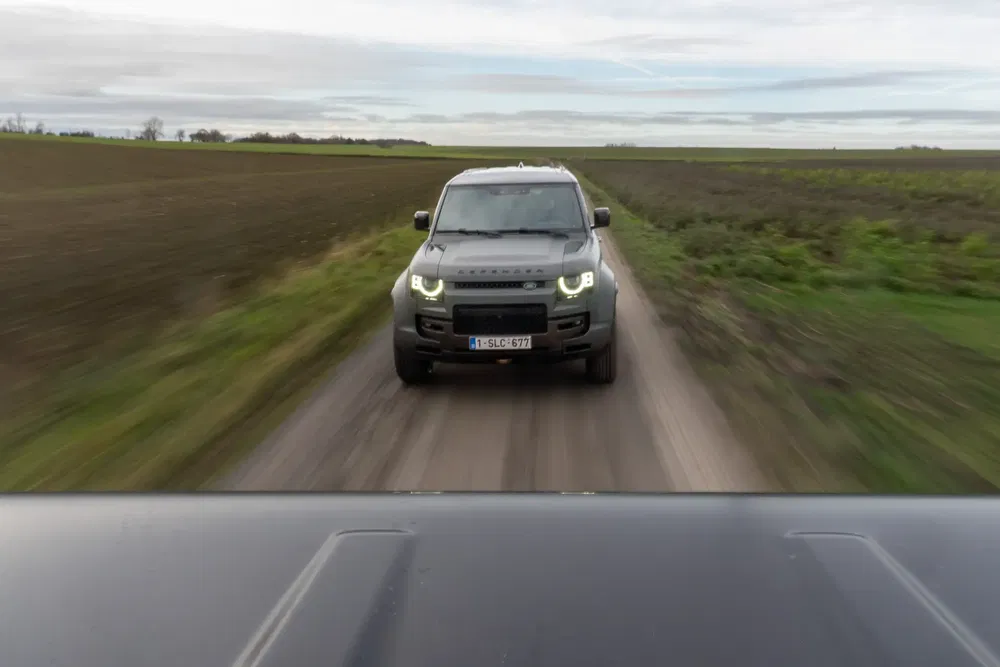 Land Rover sur chemin de campagne étroit, champs verts alentour, perspective dynamique.