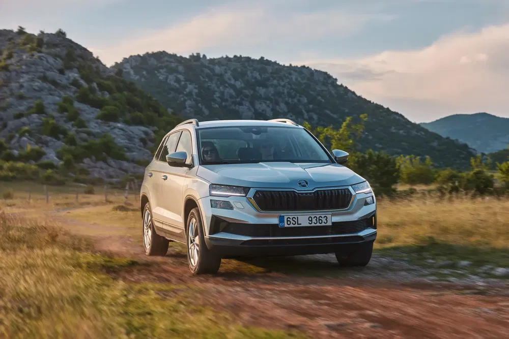 SUV Skoda Karoq 2023 sur une route de campagne avec des montagnes en arrière-plan.