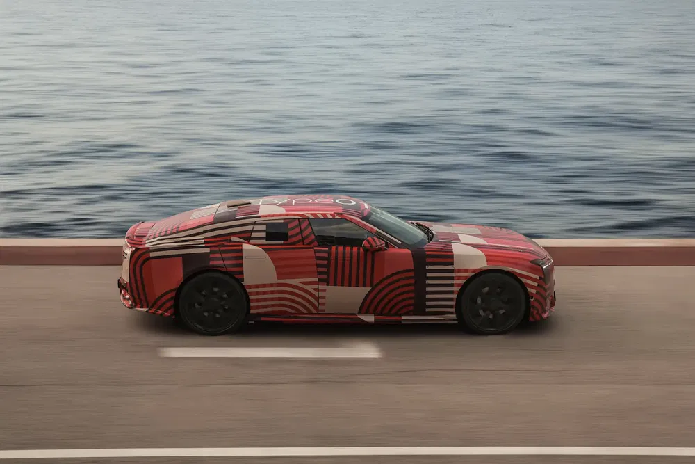 Voiture de sport camouflée, bord de mer, modèle électrique Polestar en test routier.
