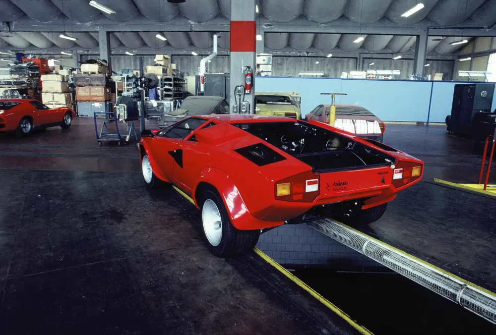 Rode Lamborghini Countach in een vintage autowerkplaats, klaar voor mechanische inspectie.