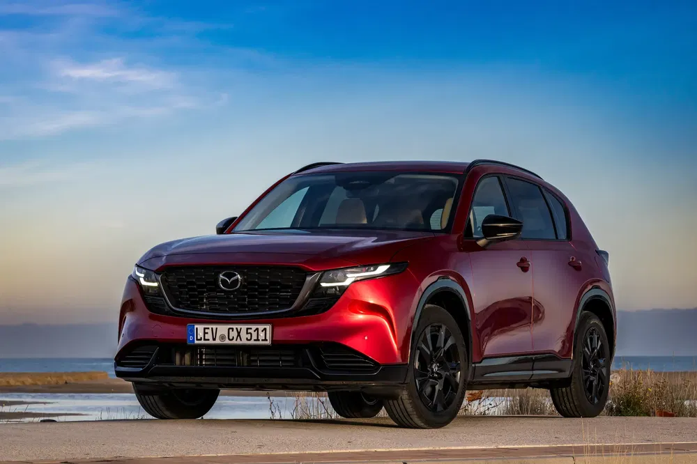 Rode Mazda CX-5 op een kustweg met een heldere lucht op de achtergrond.