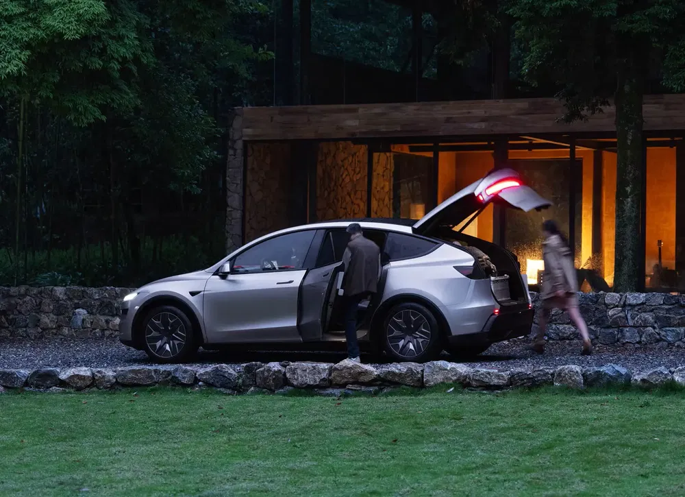 Zilveren Tesla Model X met geopende achterklep voor een moderne stenen woning.
