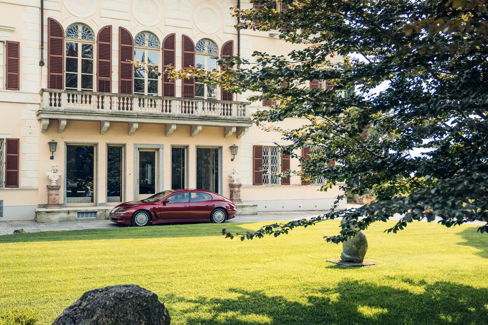 Porsche Panamera rouge stationnée devant un manoir historique avec pelouse verte.
