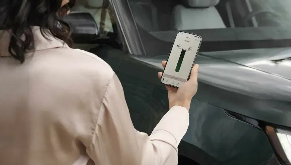 Femme utilisant une application pour surveiller l'état de charge d'un SUV vert foncé.