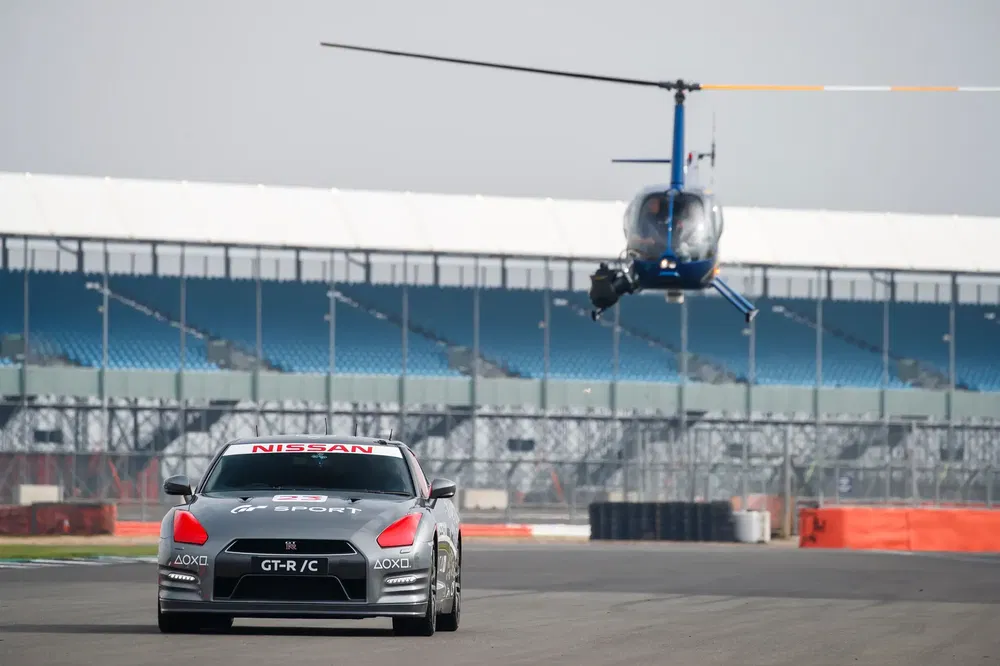 Nissan GT-R C télécommandée sur piste avec hélicoptère en arrière-plan.