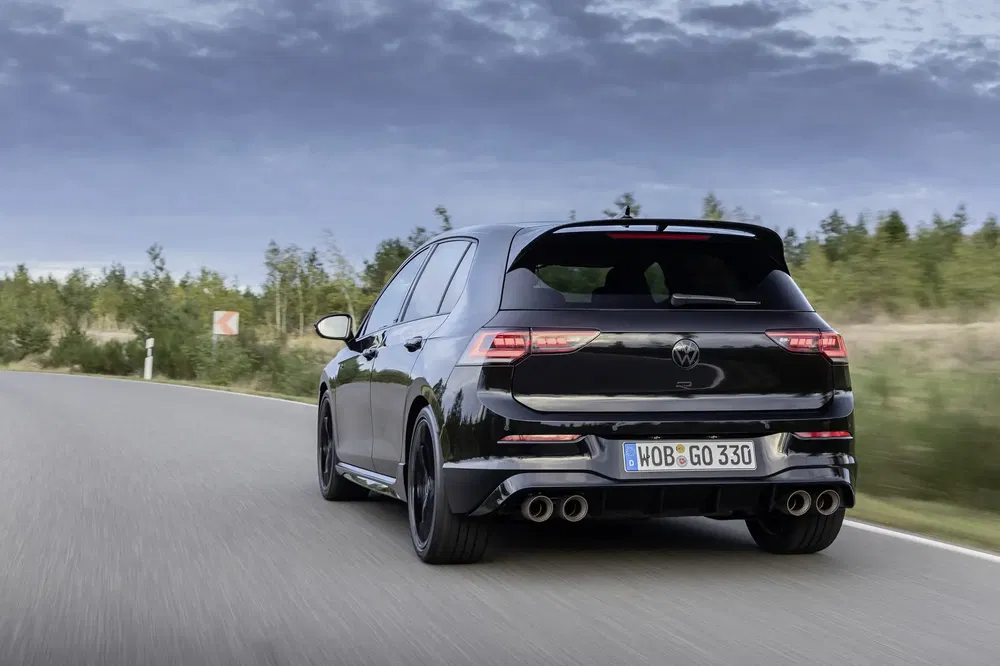 Zwarte Volkswagen Golf R op een landelijke weg omgeven door groen bos.