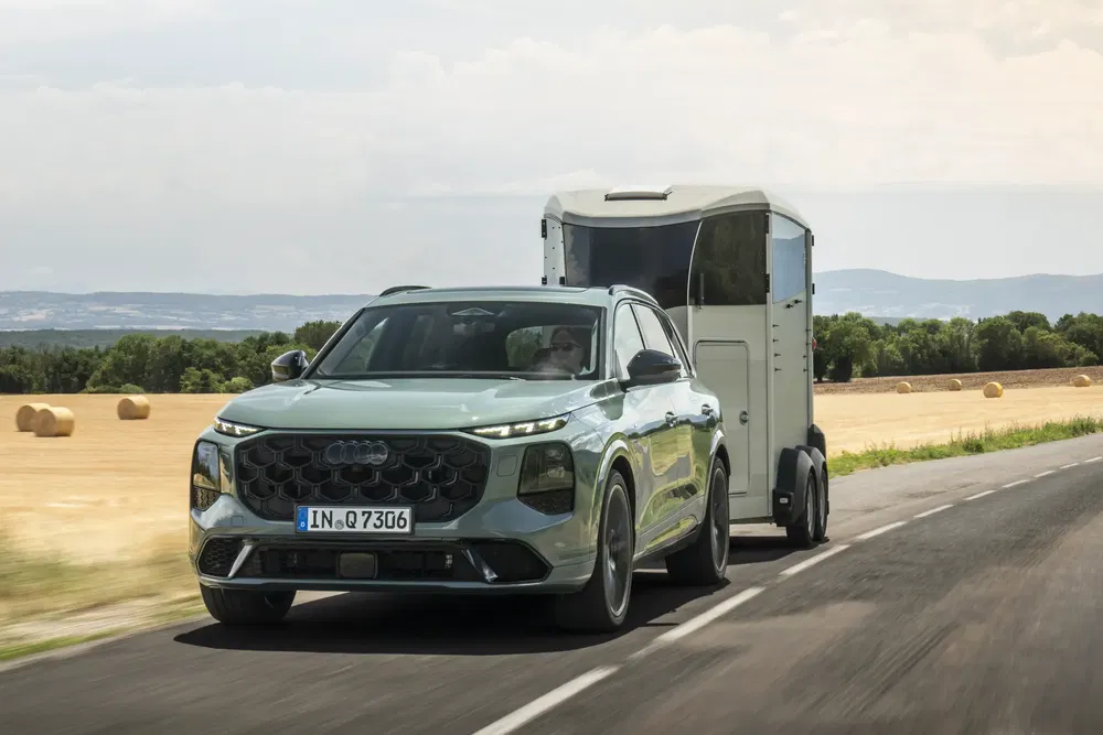 Audi Q5 2024 tractant une remorque sur une route de campagne, champs en arrière-plan.