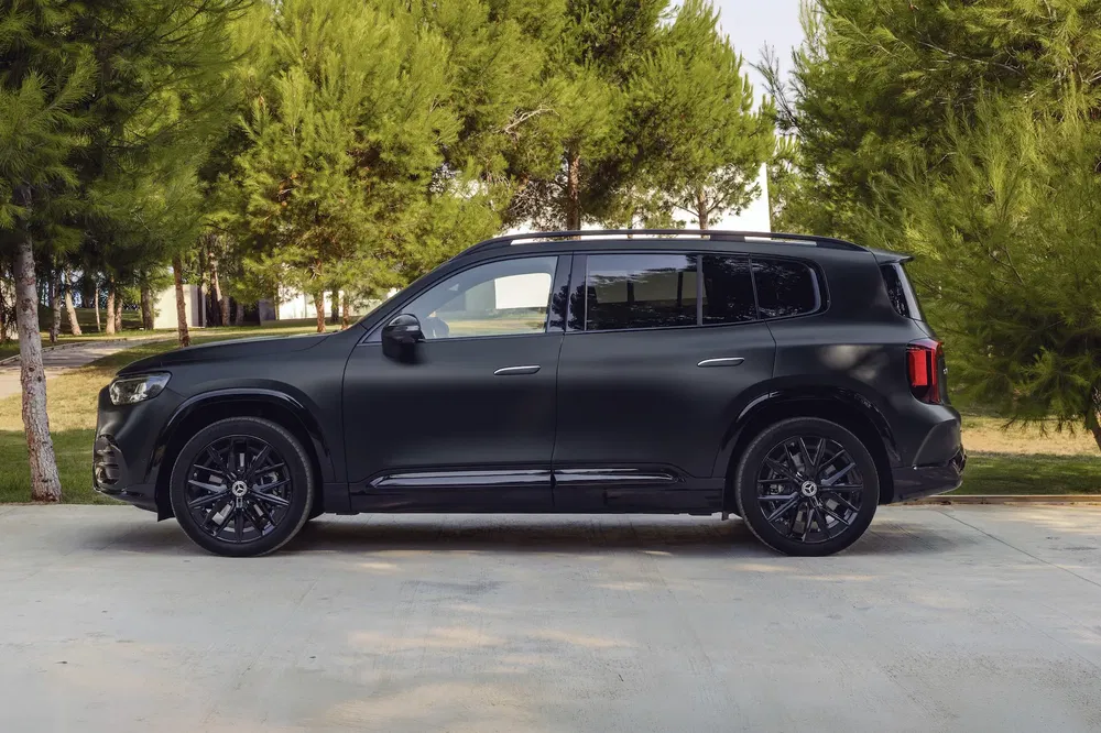 SUV noir stationné sur fond de forêt, modèle moderne avec jantes en alliage élégantes.