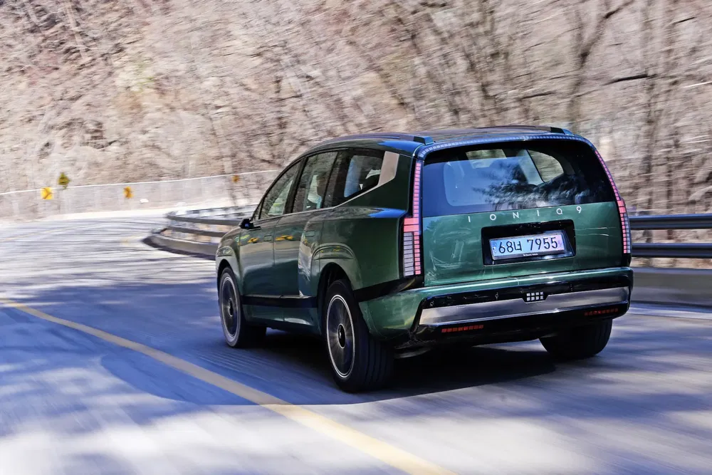 SUV Hyundai Ioniq 7 vert roulant sur une route sinueuse entourée d'arbres dénudés.