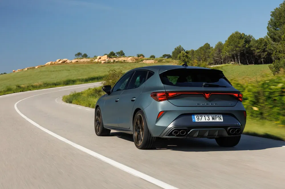 Grijze Cupra Leon 2023 rijdend op een kronkelige landelijke weg.