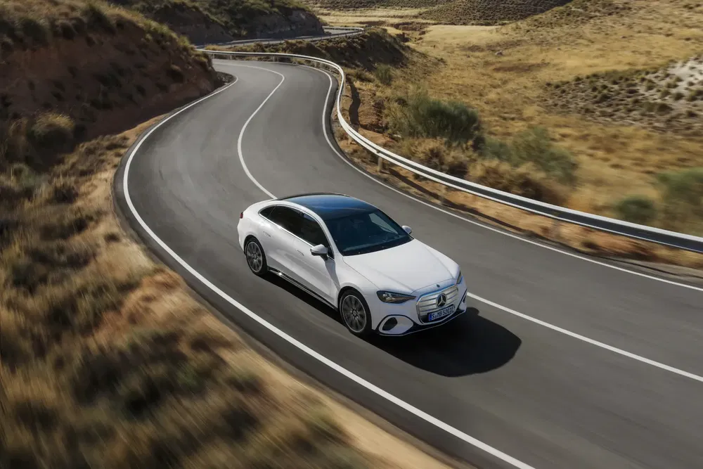 Mercedes-Benz E-Class blanche roulant sur une route sinueuse dans un paysage sec.