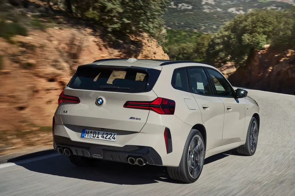 Vue arrière de la BMW X3 M sur route de montagne sinueuse, affichant son design sportif.