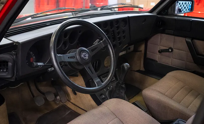 Intérieur de la Lancia Delta avec volant vintage et sièges en tissu beige.