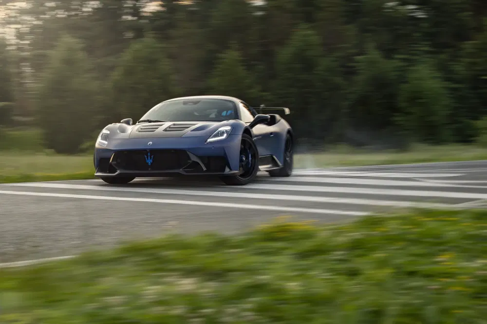 Maserati MC20 bleu roulant rapidement, virage sur route de campagne.