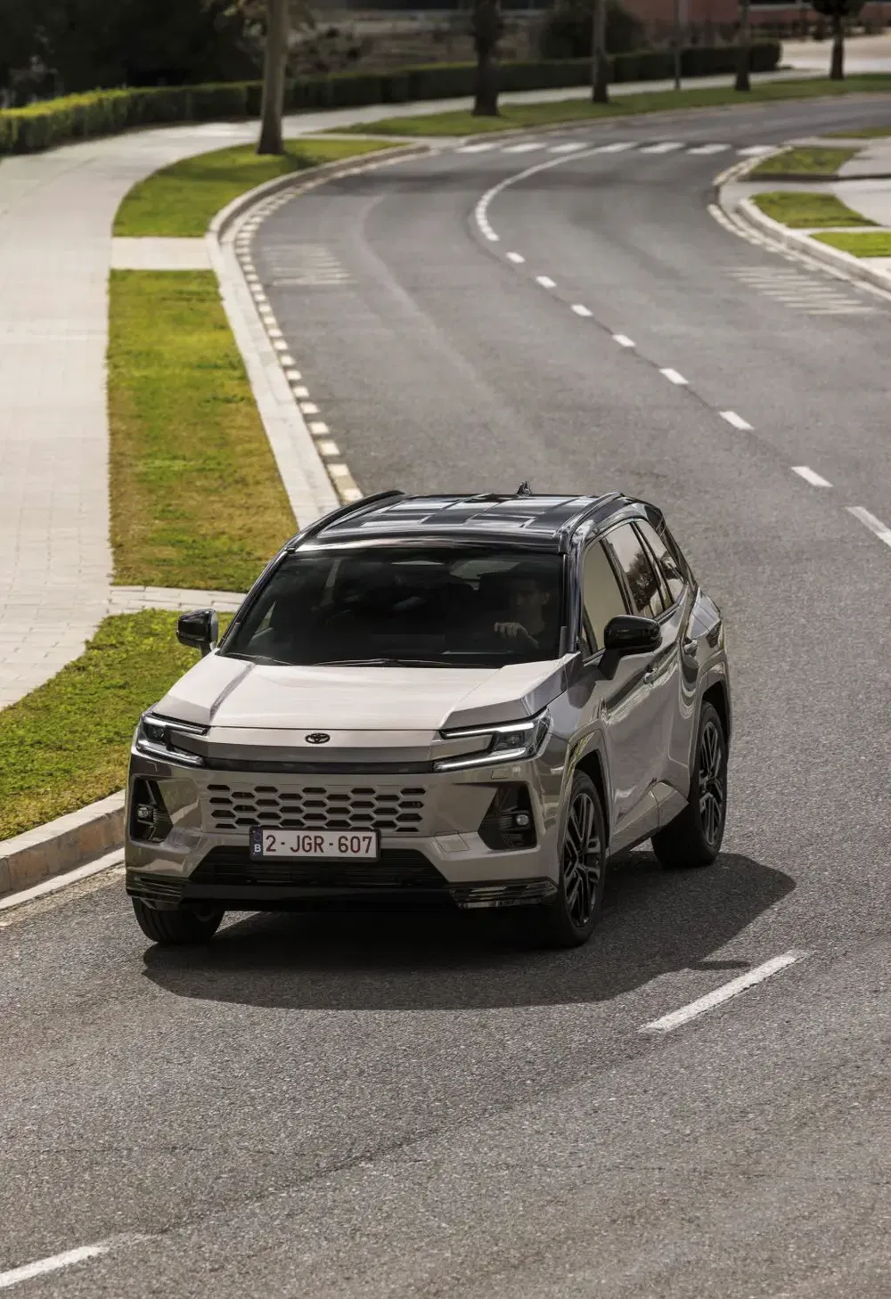 Lichtgrijze Toyota SUV rijdt op een kronkelige weg omgeven door gras.